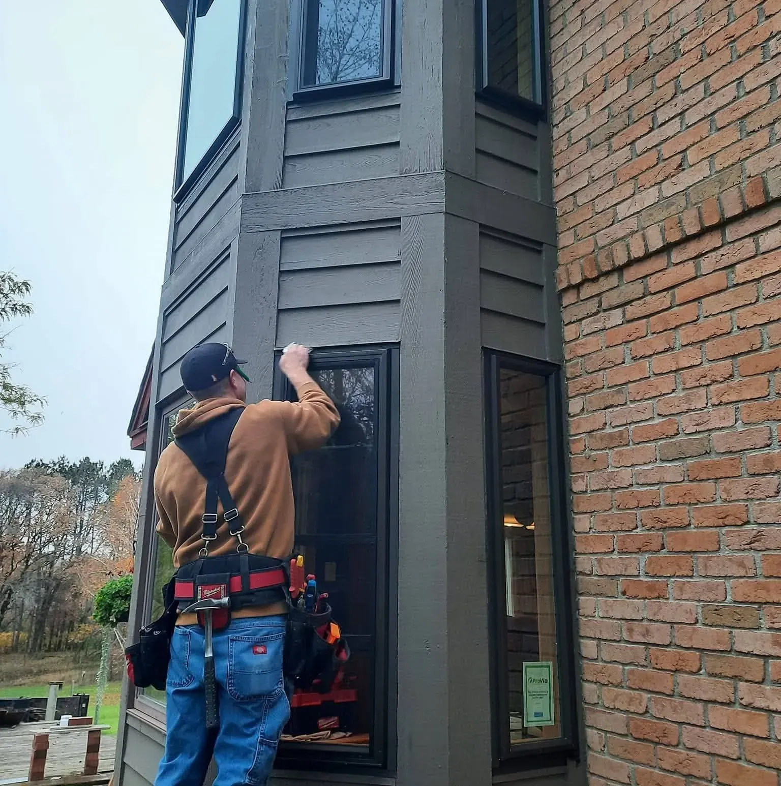 Residential window replacement in a dark exterior wall section beside a brick facade
