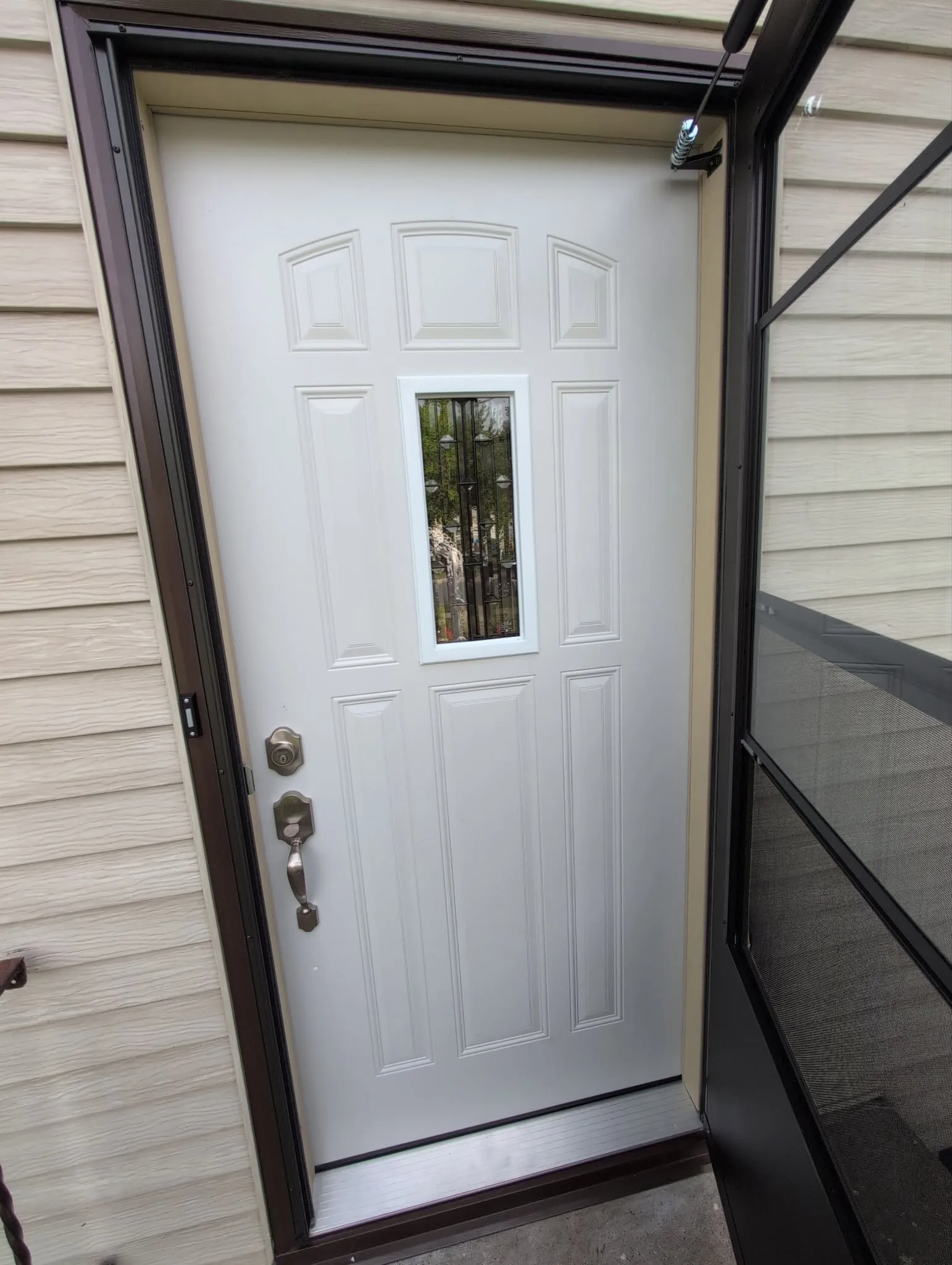 Completed white exterior entry door replacement with narrow vertical glass insert and light siding